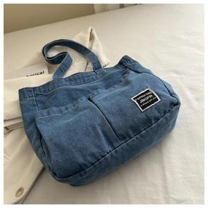 Detail of blue denim tote bag featuring dual front pockets and stitched brand label