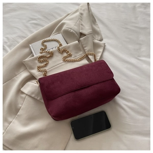 Detailed macro view of burgundy suede shoulder bag texture with golden chain on beige blazer