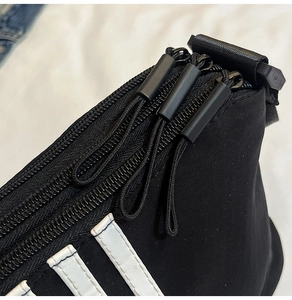 Dettaglio macro di borsa in nylon nero con tre cerniere e strisce bianche decorative