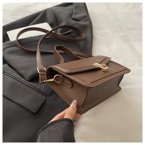 Detailed shot of brown matte PU leather shoulder bag with gold metal lock on black suit