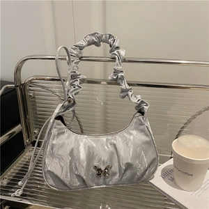 Silver pleated shoulder bag with butterfly buckle on a modern metallic glass shelf