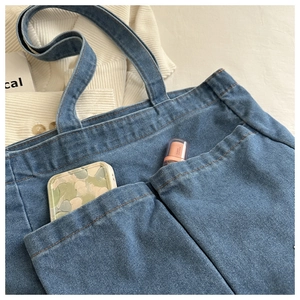 Detailed close-up of blue denim tote bag exterior pockets holding cosmetics for daily use