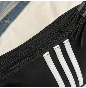 Dettaglio macro della borsa sportiva in nylon nero con tre strisce bianche e doppie cerniere
