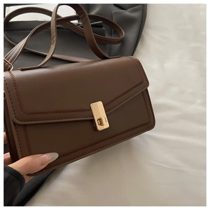 Detail of vintage brown leather handbag featuring golden metal buckle and wavy stitching