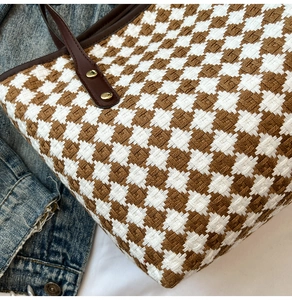 Detail of woven houndstooth tote bag with brown leather handle and gold metal rivet
