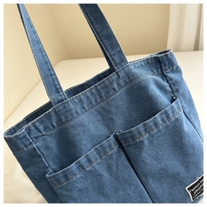 Detail of blue denim tote bag featuring dual front pockets and stitched brand logo label