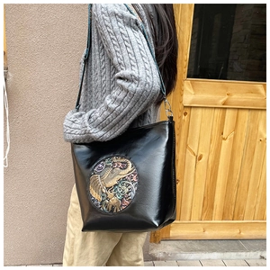 Detail of black tote bag with colorful elephant relief and wide jacquard strap on model