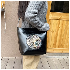 Detail of black glossy bucket bag featuring a colorful elephant relief and woven strap
