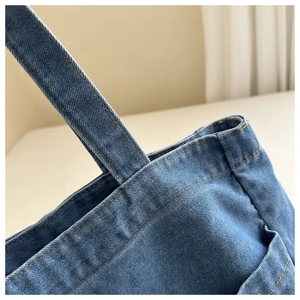 Close-up of durable blue denim fabric texture and precise stitching on tote bag handle