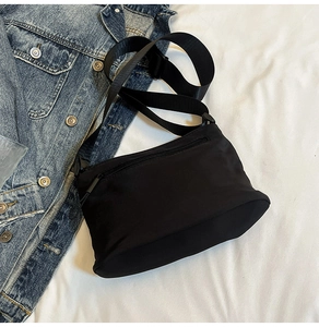 Dettaglio borsa a tracolla in nylon nero con cinturino in tessuto su fondo in tessuto bianco
