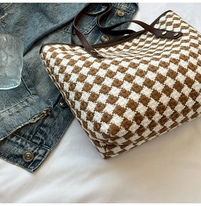 Detail of woven houndstooth tote bag featuring premium leather handles and gold rivets
