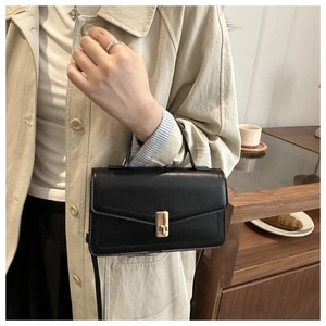 Detail of black leather envelope bag with gold twist lock and handle in cozy home setting