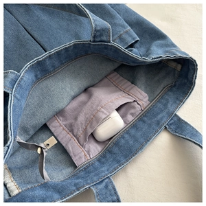 Detail of blue denim tote bag interior showing a purple pocket with wireless earphone case