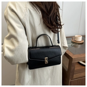 Detail of elegant black leather flap bag with gold clasp shown on a model