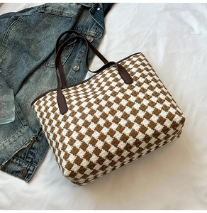Flat lay of woven houndstooth tote bag with brown leather handles on white fabric