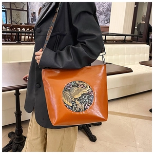 Detail of a brown leather shoulder bag featuring an elephant relief and colorful strap
