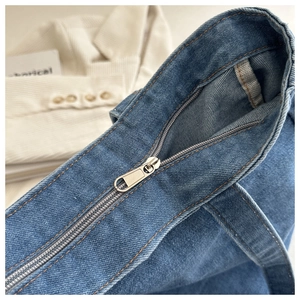 Detail of silver metal zipper and reinforced stitching on blue denim tote bag
