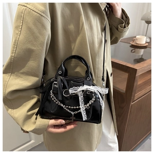 Close-up of black glossy crossbody bag with lace bow and silver chain detail