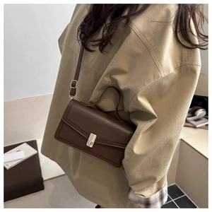 Side view of dark coffee leather shoulder bag with gold clasp worn by a model