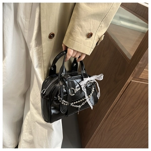 Detail of glossy black Boston bag with lace bow decoration and metallic chain handle