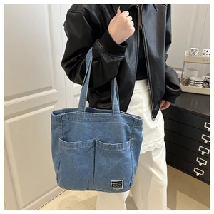 Detail of blue denim tote bag featuring dual front pockets and stitched brand label