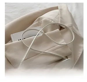Detail view of cream shoulder bag with slim cylindrical strap on beige blazer