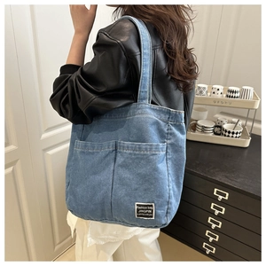 Detail of blue denim tote bag with dual front pockets and contrast stitching on a model