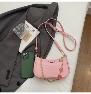 Pink crescent underarm bag with strawberry charm and metal chain on grey blazer background