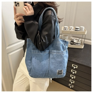 Detail of blue denim tote bag showing side pockets and woven label on washed fabric