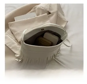 Detail showing the large capacity of the white tassel handbag with wallet and phone