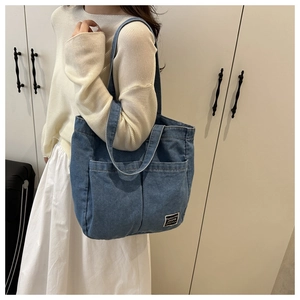 Detail of blue denim tote bag with two front pockets and woven fashion label