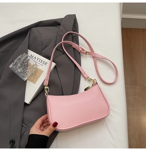 Detailed top view of pink lychee leather baguette bag on white fabric with art book
