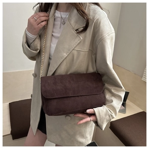 Detail of dark brown matte suede shoulder bag with gold chain strap on beige blazer