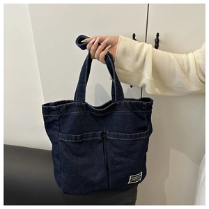 Detail shot of navy denim tote bag featuring dual front pockets and woven brand label