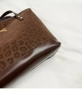 Close-up of leopard print tote bag featuring brown leather trim and golden bow logo detail