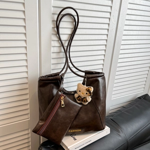 Brown large capacity tote bag with matching pouch and plush charm in elegant indoor setting