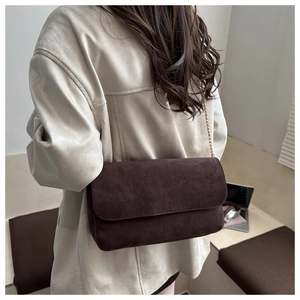 Detail view of the brown suede shoulder bag with gold chain strap worn by a model