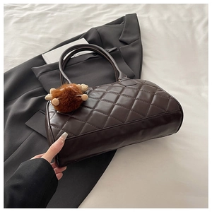 Dettaglio di una borsa bowling trapuntata marrone caffè con ciondolo di peluche su tessuto