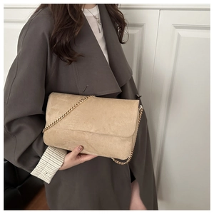 Beige suede textured flap handbag with a gold metal chain strap shown on a model
