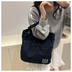 Detail of dark blue denim tote bag with fashion label shown in a casual lifestyle setting