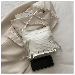 White fringe crossbody bag detail with long tassels on soft beige blazer background