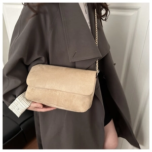 Chic beige suede crossbody bag with elegant gold chain strap worn by a model in a coat