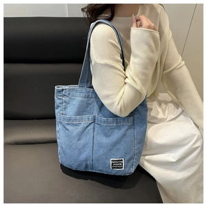 Detail of blue denim tote bag showing functional front pockets and stitched brand patch