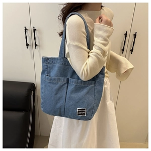 Close-up of blue denim tote bag with two front pockets and minimalist square brand patch