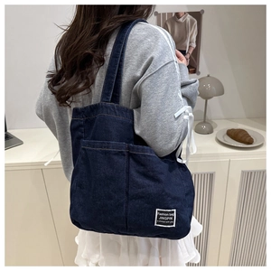 Detail of a large dark blue denim tote bag with two front pockets and logo patch