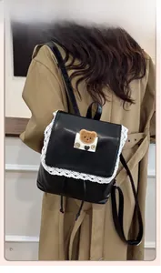 Detail view of black PU leather mini backpack featuring white lace trim and bear motif