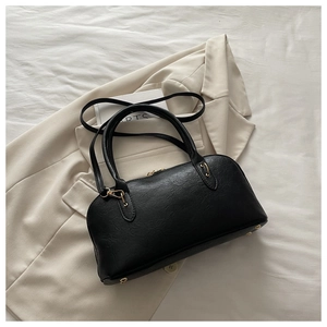 Close-up of black lychee-textured Boston bag with gold hardware on chic beige blazer