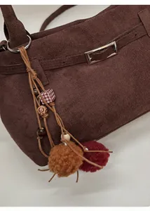 Detail of dark brown matte suede bag featuring fuzzy pom-poms and wooden bead charms