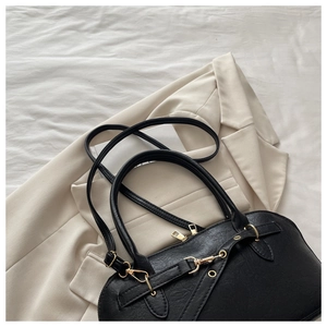 Detail view of a black retro leather bag with golden hardware on a white blazer