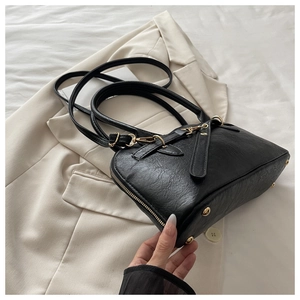 Detail of black lychee leather handbag with gold hardware on a beige blazer